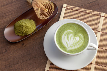 Matcha latte art heart shape on top on wooden table with some green tea powder beside and tools for tea making, Japanese style