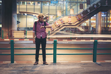 Hipster bearded man backpacker standing looking at smartwatch with car motion background while traveling at night.