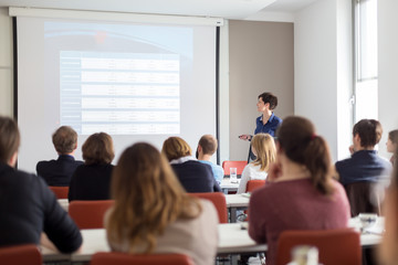 female speaker giving presentation in lecture hall at university workshop . participants listening t