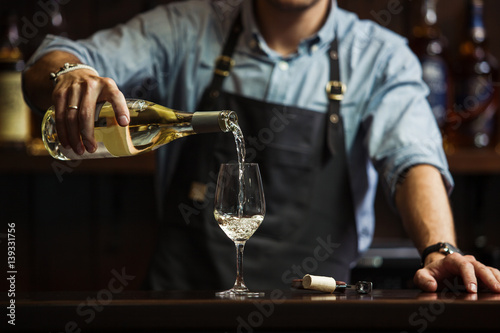 Cuadros en Lienzo Male sommelier pouring white wine into long-stemmed wineglasses.