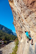 © alexbrylovhk - Mature Climber hanging on Rock above Forest and Village vertical