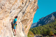 © alexbrylovhk - Mature Climber arranging Belay on Rock above Forest and Village