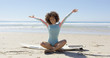 © Dash - Cheerful young woman on surfboard sitting with hands up and looking at camera in Tarifa beach.