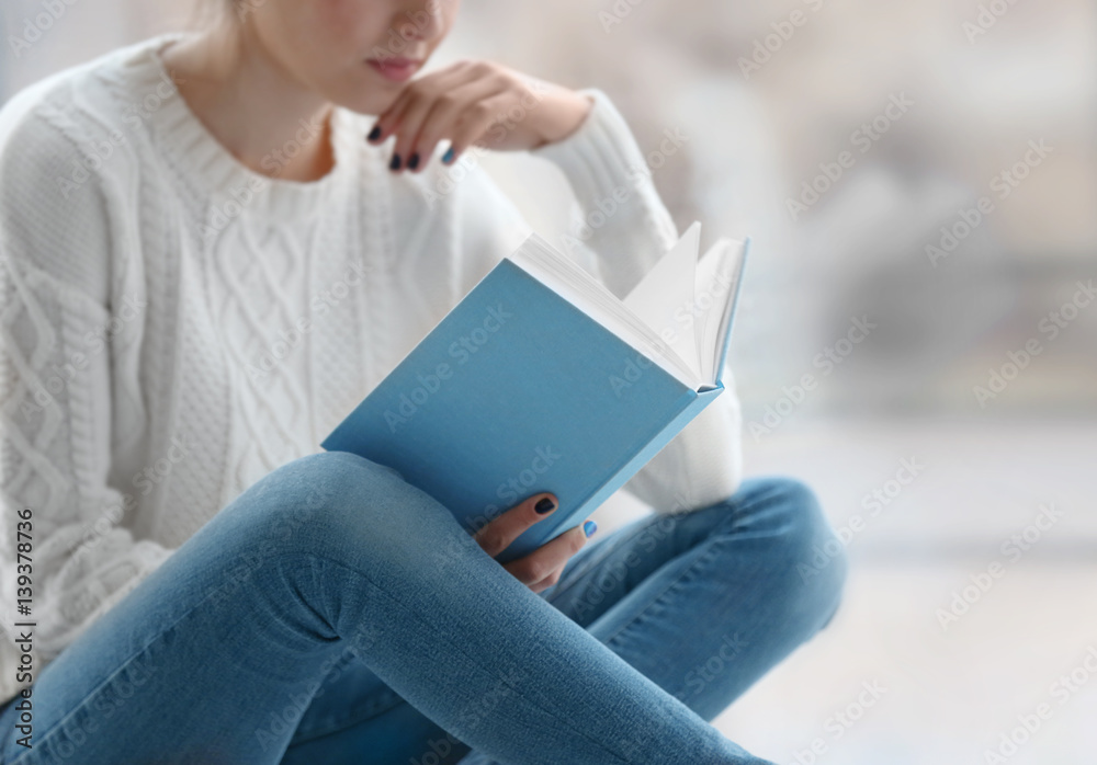 Young woman reading book on windowsill at home
