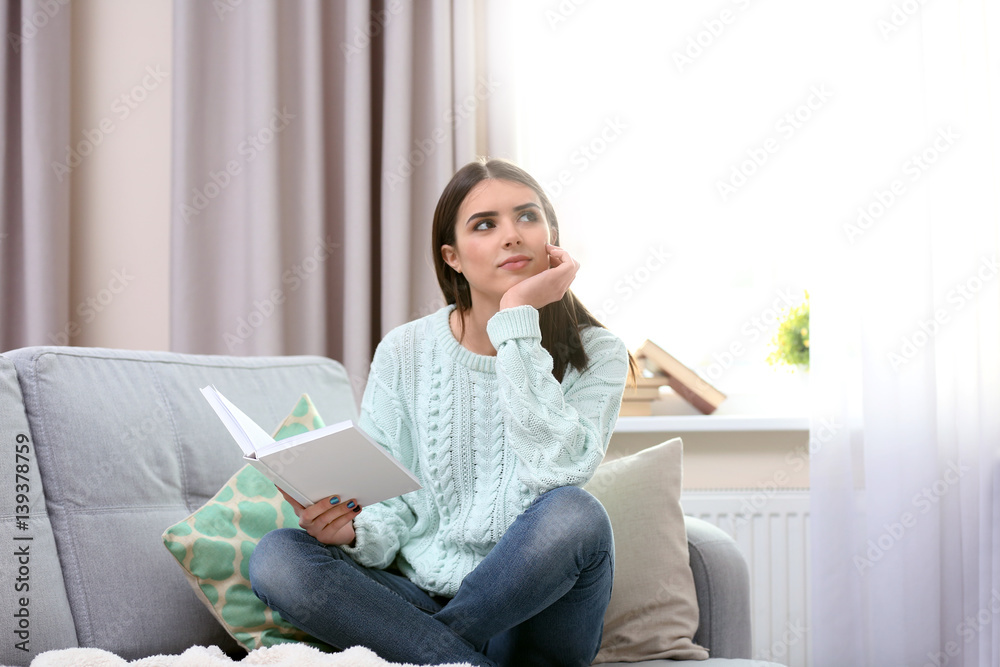 Young beautiful woman reading book at home