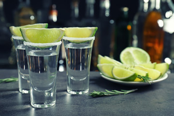 Canvas Print - Tequila shots with juicy lime slices and salt on blurred background of glass bottles