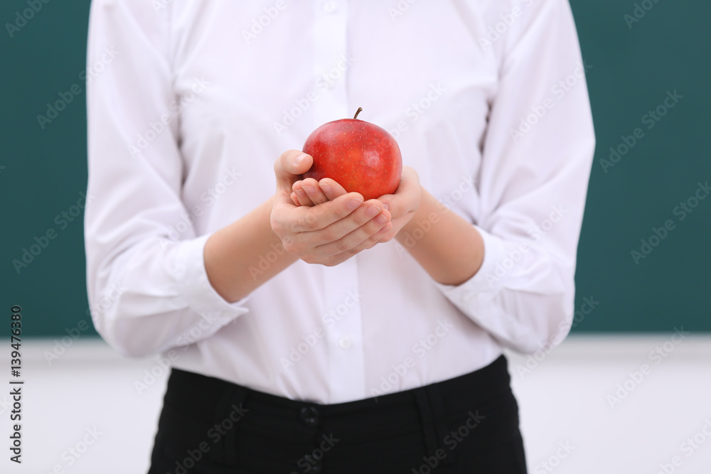 Cute schoolgirl with apple in classroom, closeup