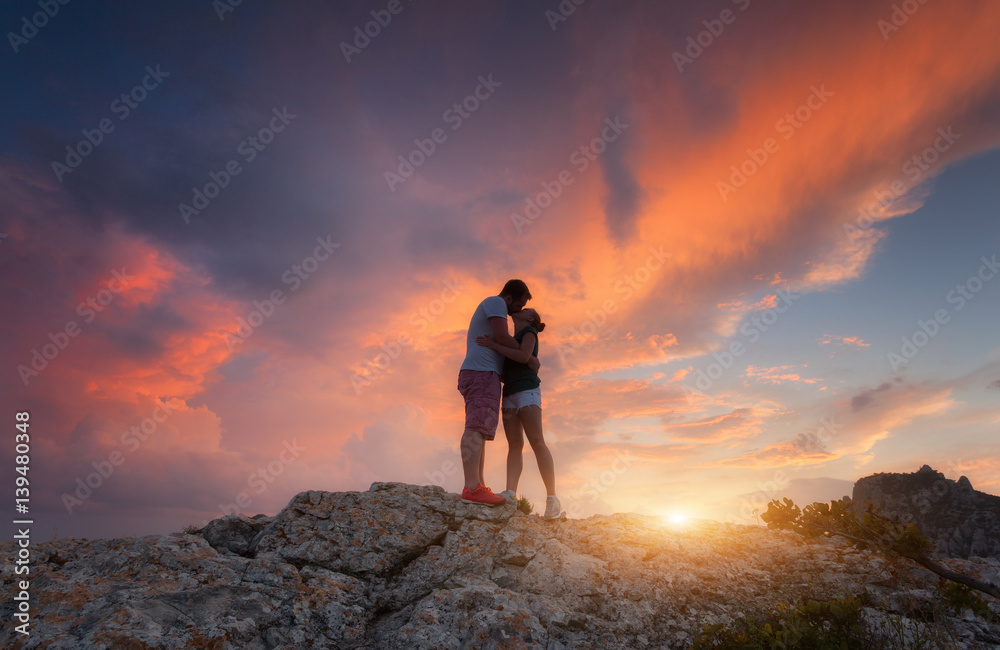 Silhouettes of a hugging and kissing man and woman on the mountain peak ...