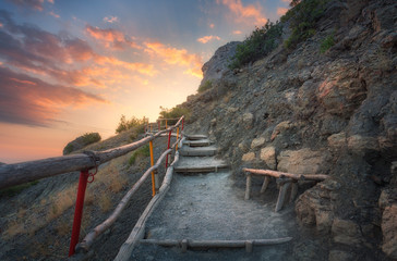 Wall Mural - Stone stairs with wooden railing in the mountains at sunset. Landscape with mountain path and rocks against colorful blue sky with clouds. Trail leading to the mountain peak. Adventure and travel  
