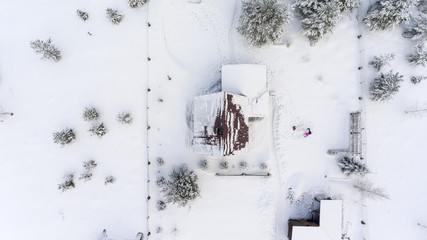 Wall Mural - Top view at the timber house under snow in countryside. Courtyard with people playing in snowdrift.