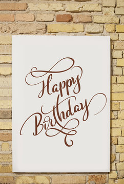 brick wall and white sheet and text Happy Birthday. Calligraphy lettering