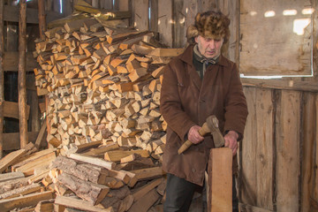 elderly old man in a cap with earflaps andfelt boots chops firewoods