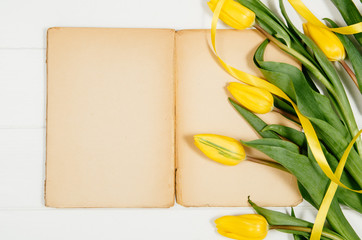 Poster - Background with yellow tulips, blank notepad on white wooden table top view. Creative woman's workspace concept with copy space. Product photograph taken from above with frame composition