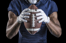Close Up View Of An American Football Player Holding A Football. Selective Focus On The Laces Of The Football And The Wide Receiver Gloves. Shot On A Black Background