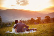 happy loving couple sitting on plaid in field. background mountains.