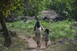 A young mother and children walking away through open forest on a small dirt path. 
