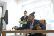 © cineberg - African American office worker with collected rasta hair at work. On background, Asian colleague standing holding documents. Selective focus
