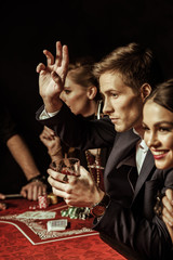 elegant young smiling people drinking alcohol at poker table on black