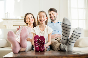 Wall Mural - smiling daughter sitting with hugging parents on sofa at home