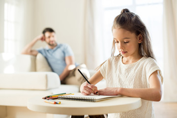 Wall Mural - portrait of focused daughter drawing picture with father behind