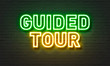 Guided tour neon sign on brick wall background.