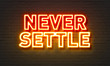 Never settle neon sign on brick wall background.
