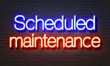 Scheduled maintenance neon sign on brick wall background.