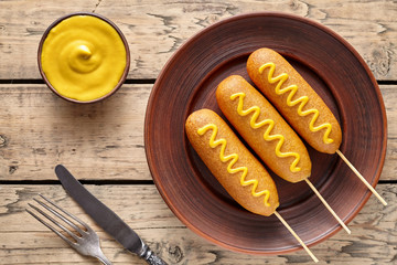 Corn dog traditional American fast food fried sausages in cornmeal batter on stick with mustard snack treat on rustic wooden table