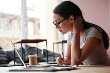 Sticker - Pretty young caucasian woman using laptop computer and writing notes.