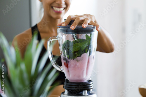 Cuadros en Lienzo Woman blending spinach, berries, bananas and almond milk to make a healthy green