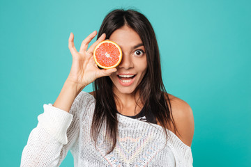 Poster - Cheerful amusing young woman covered her eye with grapefruit half