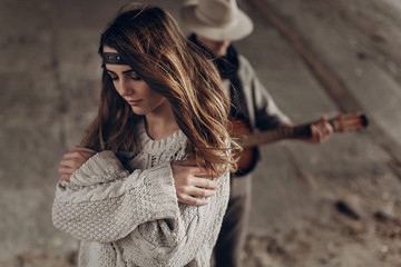 Wall Mural - Beautiful sensual indie girl in hipster boho clothes posing in front of handsome cowboy guitar player outdoors