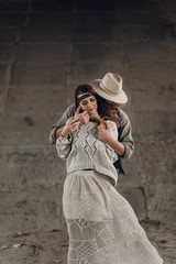 Wall Mural - Handsome cowboy man in white hat touching cheek of beautiful boho gypsy woman with leather headband, posing outdoors