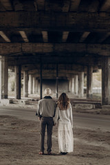 Wall Mural - Handsome texas cowboy man in white hat holding hands with beautiful gypsy woman in white dress, couple walking in the city