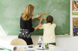 © PhotoAlto - Teacher helping boy draw angle on blackboard using protractor, rear view