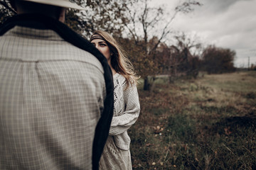 Wall Mural - Stylish hipster man in cowboy shirt and hat looking at emotional gypsy hipster woman, autumn field background