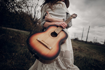 Wall Mural - Hipster musician couple hugging in field, handsome man embracing gypsy woman in white dress, guitar closeup