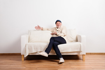 Wall Mural - Senior man in beige sweater sitting on sofa, studio shot.