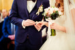 Groom in stylish blue suit puts wedding ring on bride's finger