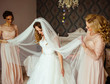 Bridesmaids in pink dresses hold bride's veil while they stand in the room