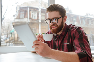 Wall Mural - Attractive bearded young man using tablet computer.