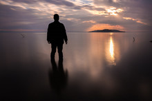 Long Exposure Shot Of A Silhouette Of A Man In Water In Front Of A Sunset