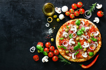 Food ingredients and spices for cooking mushrooms, tomatoes, cheese, onion, oil, pepper, salt, basil, olive and delicious italian pizza on black concrete background. Copyspace. Top view.