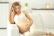 © Africa Studio - Young pregnant woman with headphones on the sofa
