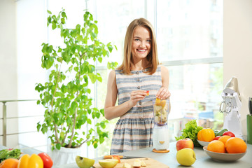 Wall Mural - Young woman making fresh juice in the kitchen