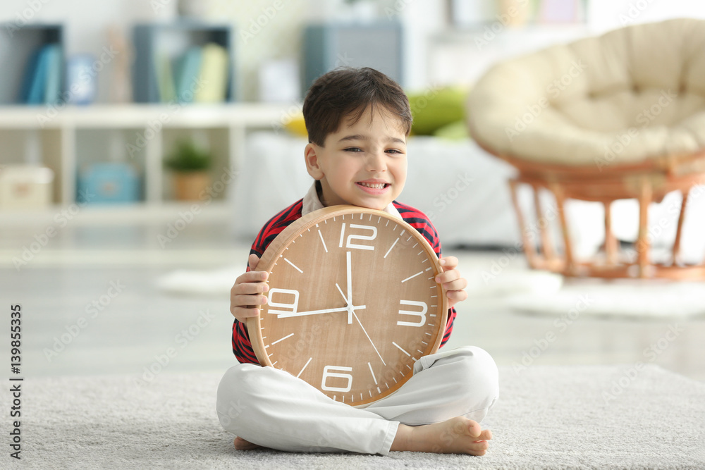Cute little boy with big clock sitting on floor at home