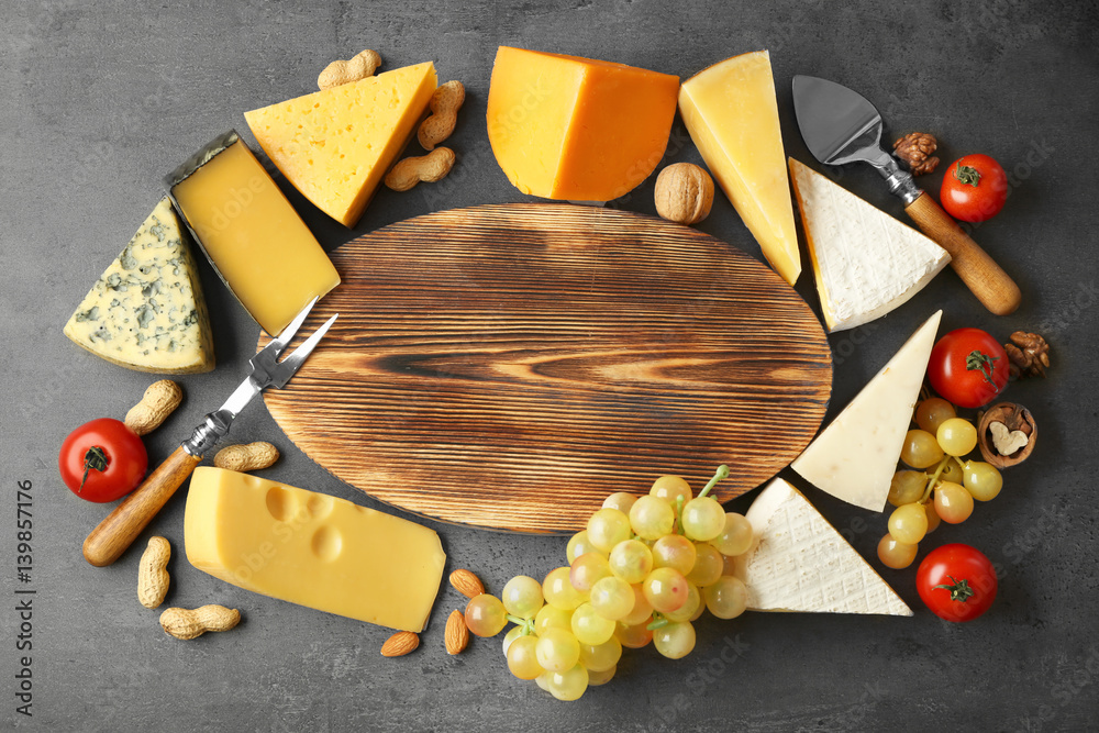 Variety of cheese and nuts around cutting board on dark background