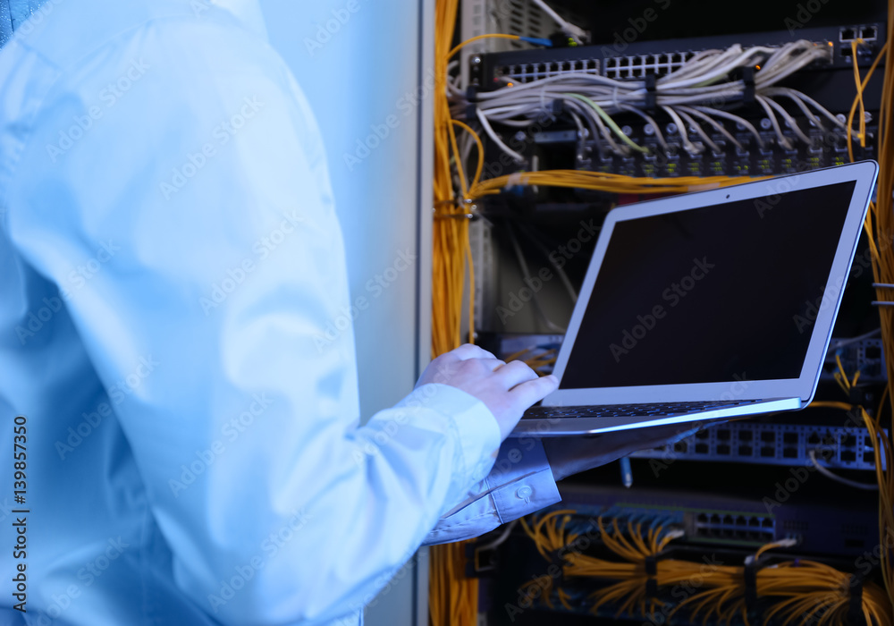 Handsome young engineer with laptop in server room