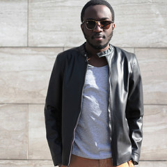 Wall Mural - Fashion african man wearing a sunglasses, black rock leather jacket over textured gray background evening in city