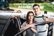 © F8  \ Suport Ukraine - Beautiful young couple is smiling and looking at camera while leaning on their new car in a motor show. Man is holding car keys